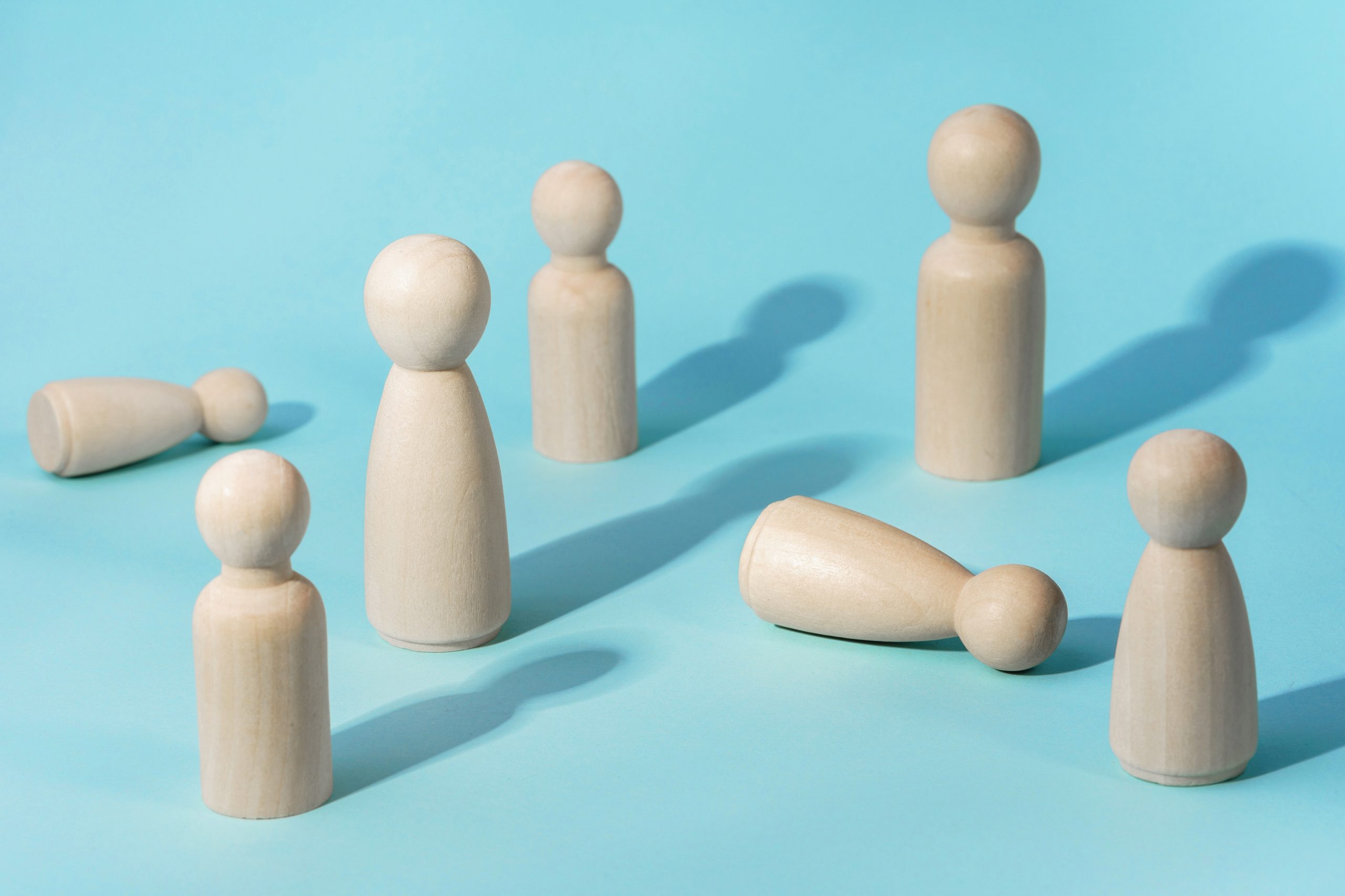 Houten poppetjes in een groep, met één figuurtje dat omgevallen op de grond ligt – metafoor voor spanning en onveiligheid in een team.